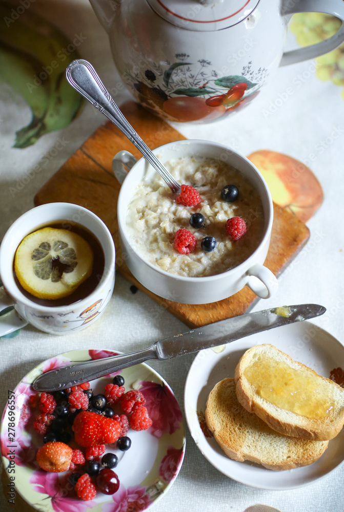 breakfast still life with oatmeal, seasonal berries, roasted toasts with lemon jam cup of tea spoon and knife