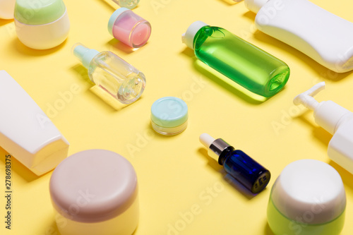 Composition of different sized cosmetic jars and bottles on yellow background. Beauty care concept with copy space
