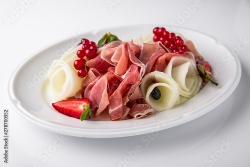 Slicing gourmet meat, prosciutto from beef and pork with berries, cheese, vegetables. Banquet festive dishes. Gourmet restaurant menu. White background.