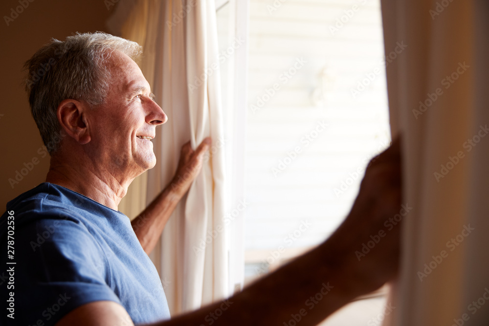 Smiling senior white man opening the curtains on a sunny morning, side view, close up Smiling senior white man opening the curtains on a sunny morning, side view, close up