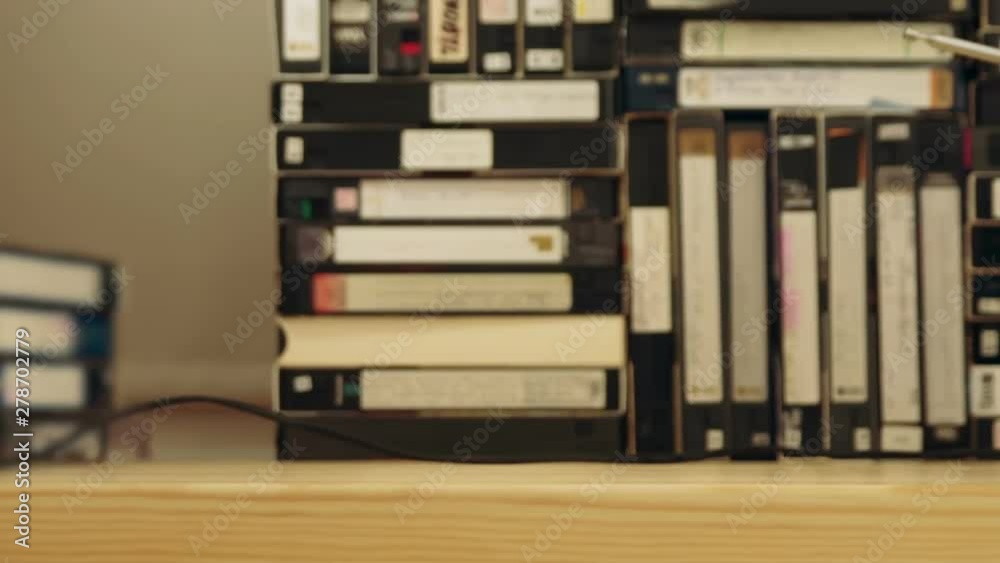 Old small TV set with antenna against background made of VHS and S-VHS video tapes. Camera moving horizontally until TV set is in frame. Tracking shot Old small TV set with antenna against background made of VHS and S-VHS video tapes. Camera moving horizontally until TV set is in frame. Tracking shot