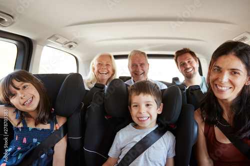 Three generation white family sitting in two rows of passenger seats in a car, smiling to camera