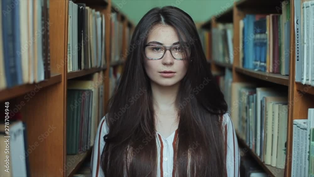 Portrait ofpretty beautiful girl in library with long black hair. Female student studying among lot of books between shelfs. Portrait ofpretty beautiful girl in library with long black hair. Female student studying among lot of books between shelfs.