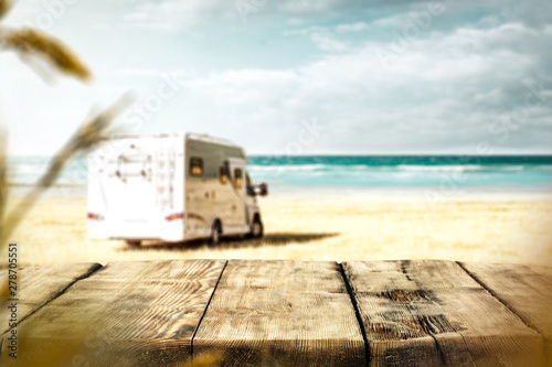 Table background with a wooden board and sunny beach and ocean and a camper van