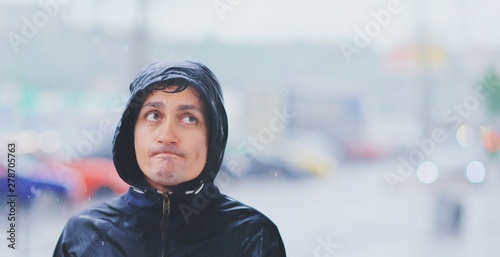 Foto Portrait of a young wet man in a jacket with a hood in the rain on blurred background city street in tsunami, close-up