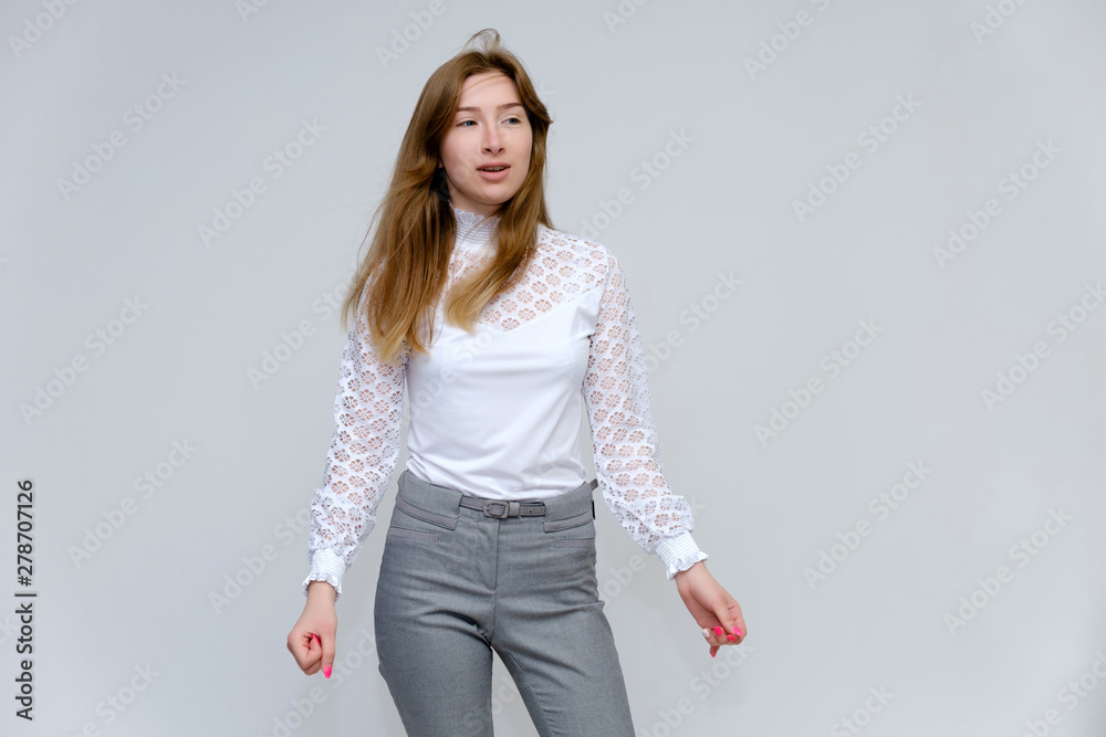 Portrait of a knee-high young pretty brunette girl woman with beautiful long hair on a white background in a white jacket and gray pants. He talks, shows his hands with emotions in various poses. Portrait of a knee-high young pretty brunette girl woman with beautiful long hair on a white background in a white jacket and gray pants. He talks, shows his hands with emotions in various poses.