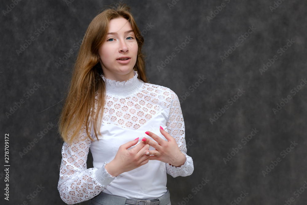 Portrait to the waist of a young pretty brunette girl woman with beautiful long hair on a gray background in a white jacket. He talks, smiles, shows his hands with emotions in various poses. Portrait to the waist of a young pretty brunette girl woman with beautiful long hair on a gray background in a white jacket. He talks, smiles, shows his hands with emotions in various poses.
