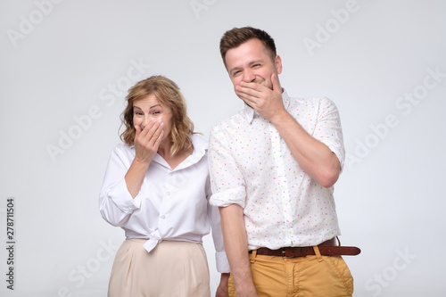 Mature woman and man giggling together covering their mouths with hands trying to be calm