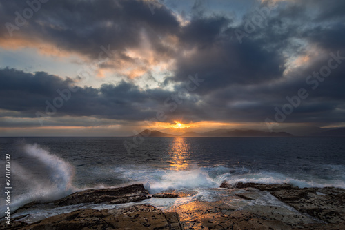 Sunset with storm over Mount Louro with storm approaching and sea beaten with waves in tide rising over the rocks of La Sagrada in summer in Porto do Son, A Coruña, Galicia, Spain.