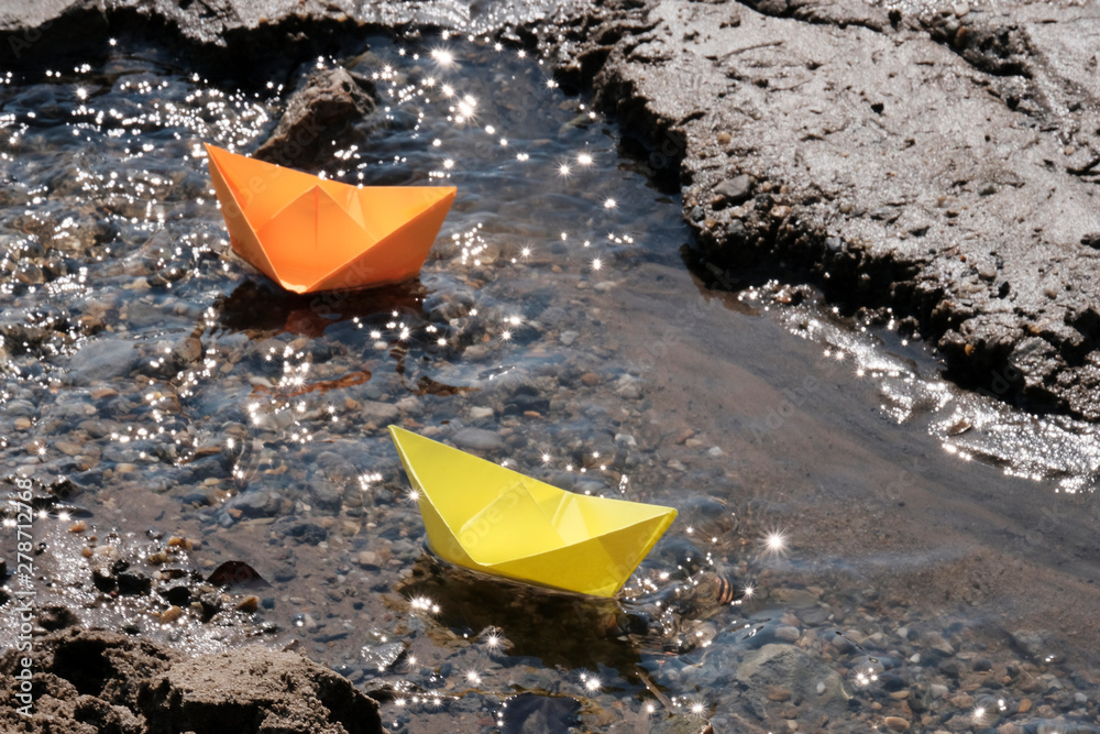 Orange and yellow paper boats floating on the spring stream. Origami toys for children. Orange and yellow paper boats floating on the spring stream. Origami toys for children.