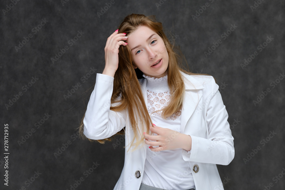 Portrait to the waist of a young pretty brunette girl woman with beautiful long hair on a gray background in a white jacket. He talks, smiles, shows his hands with emotions in various poses. Portrait to the waist of a young pretty brunette girl woman with beautiful long hair on a gray background in a white jacket. He talks, smiles, shows his hands with emotions in various poses.