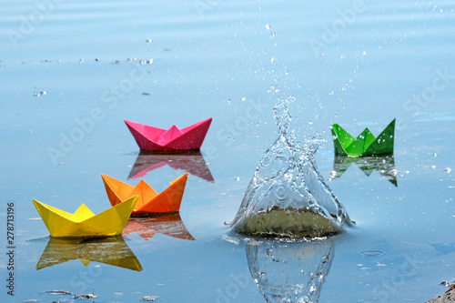 Colorful paper boats in the spring river. The result of a successful business. Origami toys for children.