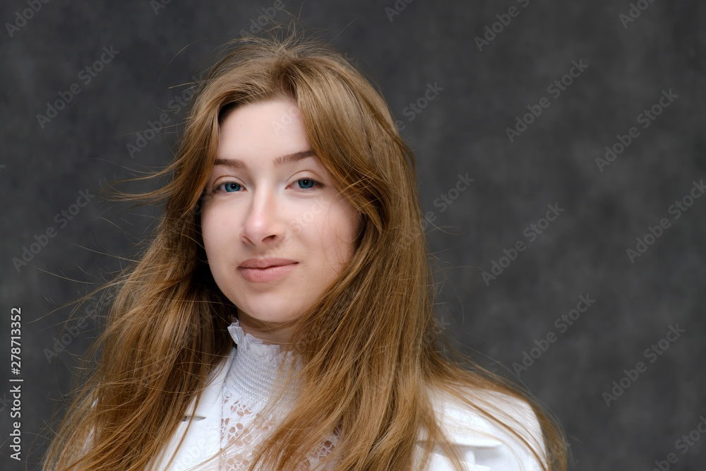 Fototapeta premium Close-up portrait of a young pretty brunette girl woman with beautiful long hair on a gray background in a white jacket. He talks, smiles, shows his hands with emotions in various poses.