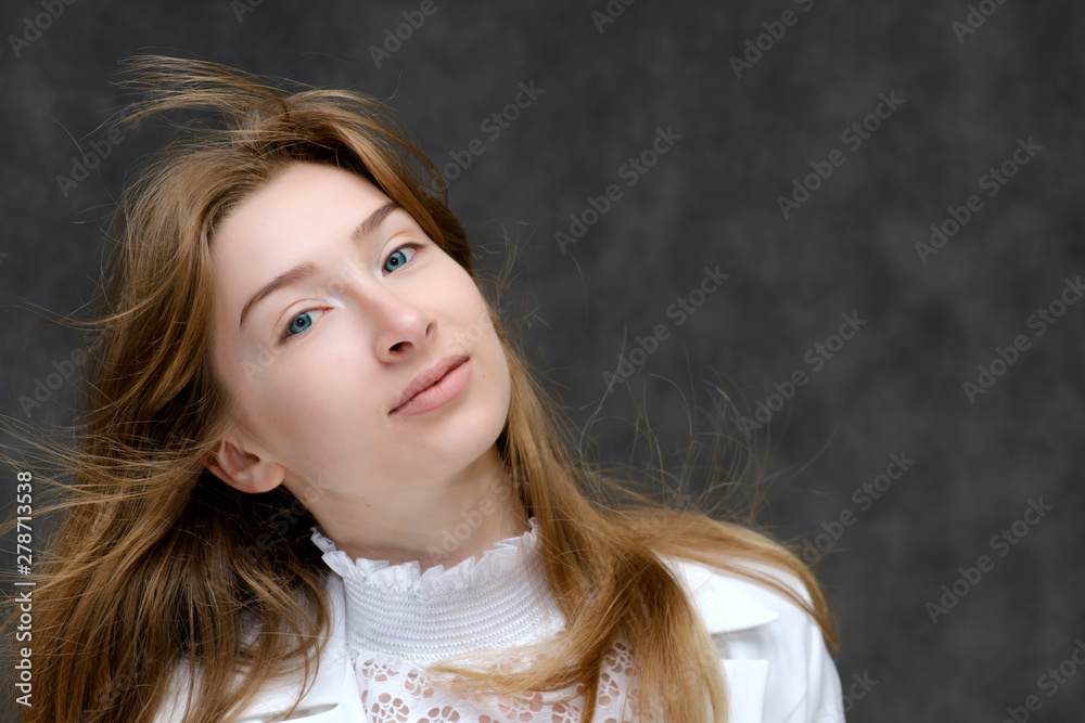 Fototapeta premium Close-up portrait of a young pretty brunette girl woman with beautiful long hair on a gray background in a white jacket. He talks, smiles, shows his hands with emotions in various poses.