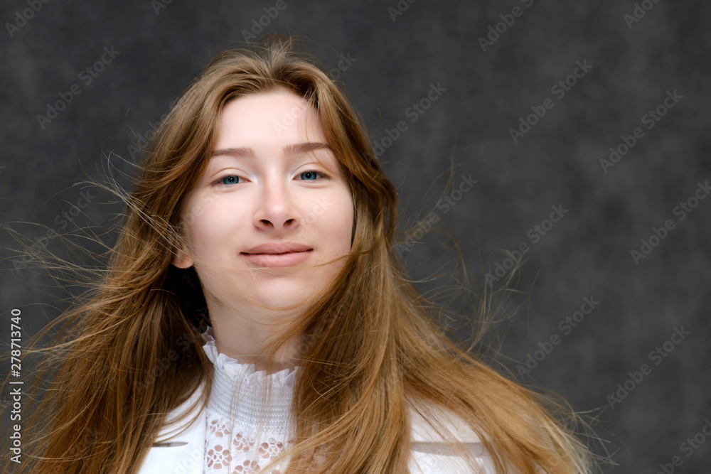 Close-up portrait of a young pretty brunette girl woman with beautiful long hair on a gray background in a white jacket. He talks, smiles, shows his hands with emotions in various poses. Close-up portrait of a young pretty brunette girl woman with beautiful long hair on a gray background in a white jacket. He talks, smiles, shows his hands with emotions in various poses.