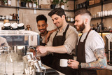 Three cheerful male baristas standing at the coffee shop