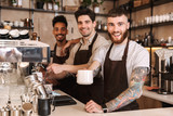 Three cheerful male baristas standing at the coffee shop