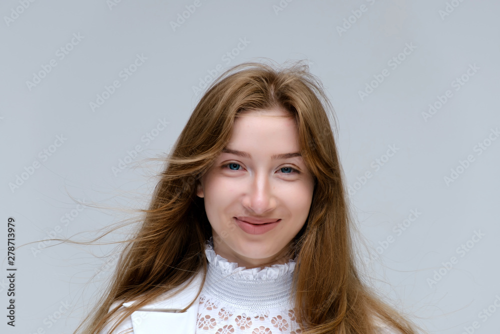Fototapeta premium Close-up portrait of a young pretty brunette girl woman with beautiful long hair on a white background in a white jacket. He talks, smiles, shows his hands with emotions in various poses.