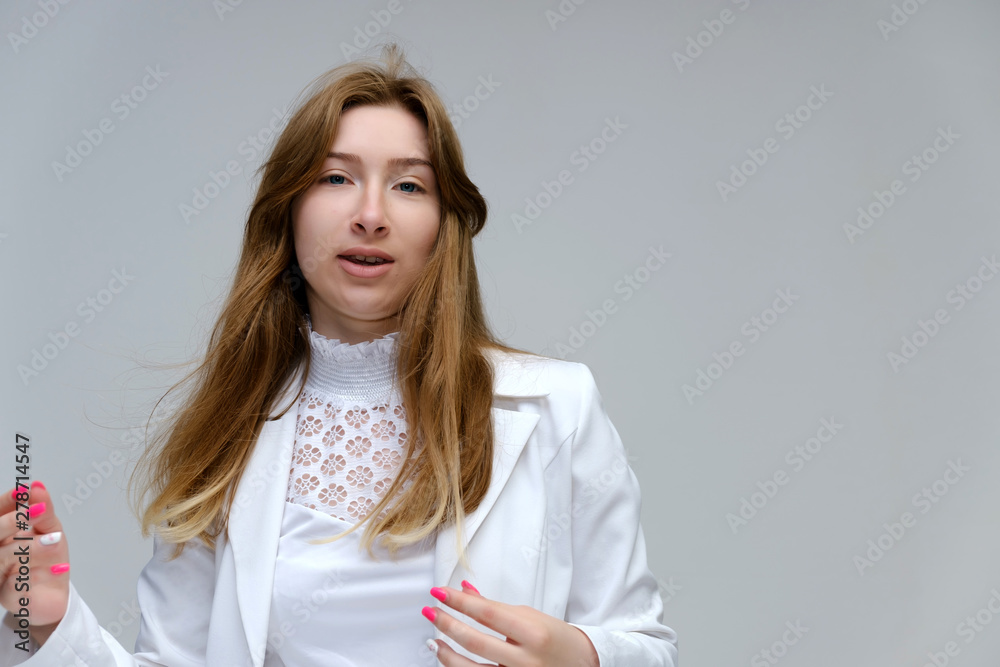 Portrait to the waist of a young pretty brunette girl woman with beautiful long hair on a white background in a white jacket. He talks, smiles, shows his hands with emotions in various poses. Portrait to the waist of a young pretty brunette girl woman with beautiful long hair on a white background in a white jacket. He talks, smiles, shows his hands with emotions in various poses.