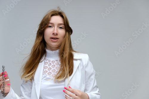 Portrait to the waist of a young pretty brunette girl woman with beautiful long hair on a white background in a white jacket. He talks, smiles, shows his hands with emotions in various poses.