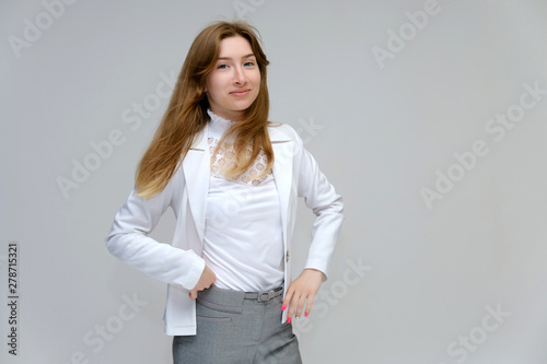 Portrait to the waist of a young pretty brunette girl woman with beautiful long hair on a white background in a white jacket and gray pants. Talks, smiles, shows hands with emotions in various poses.