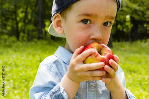Funny kid eating a big red apple outdoors. Closeup	