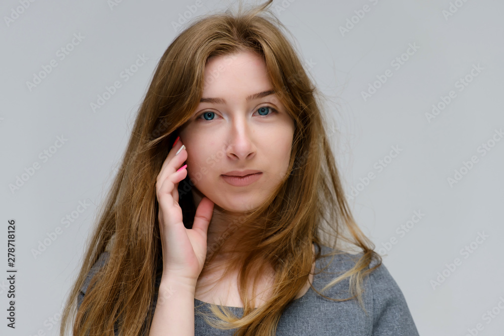 Close-up portrait of a young pretty brunette girl woman with beautiful long hair on a white background in a gray dress. He talks, smiles, shows his hands with emotions in various poses. Close-up portrait of a young pretty brunette girl woman with beautiful long hair on a white background in a gray dress. He talks, smiles, shows his hands with emotions in various poses.