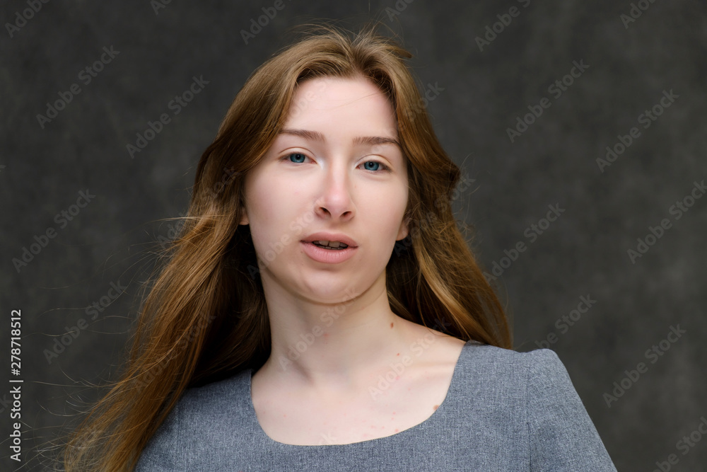 Close-up portrait of young pretty brunette girl woman with beautiful long hair on gray background in gray dress. He talks, smiles, shows his hands with emotions in various poses. Close-up portrait of young pretty brunette girl woman with beautiful long hair on gray background in gray dress. He talks, smiles, shows his hands with emotions in various poses.