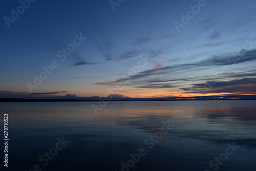 Dark blue sky in the twilight glow of sunset is reflected in the quiet surface of the water of the lake