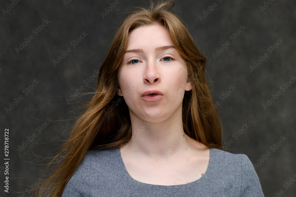 Close-up portrait of young pretty brunette girl woman with beautiful long hair on gray background in gray dress. He talks, smiles, shows his hands with emotions in various poses. Close-up portrait of young pretty brunette girl woman with beautiful long hair on gray background in gray dress. He talks, smiles, shows his hands with emotions in various poses.