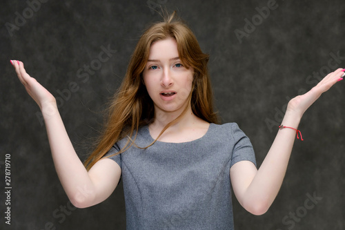 Portrait below the chest of a young pretty brunette girl woman with beautiful long hair on a gray background in a gray dress. He talks, smiles, shows his hands with emotions in various poses.