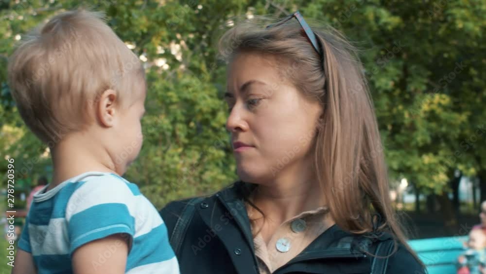 Unhappy kid sitting on the mother's hands. Mom with toddler on a stroll. Parenthood concept Unhappy kid sitting on the mother's hands. Mom with toddler on a stroll. Parenthood concept