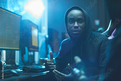 Content creative young Afro-American coding specialist in hoodie gesturing hands while discussing web script with colleague