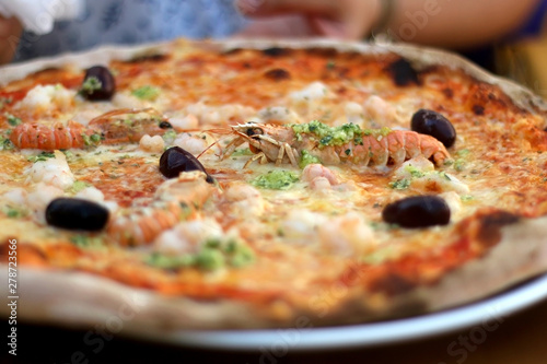 Pizza with tomato sauce, cheese, shrimps, olives and pesto. Selective focus.