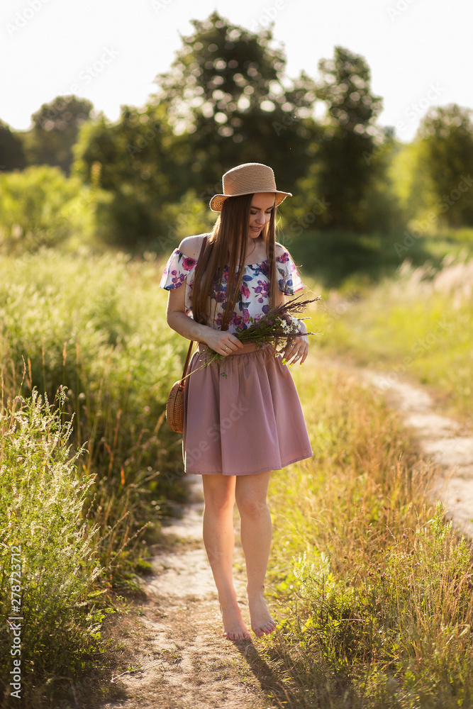 a slender girl in a straw hat and with a straw handbag holding a bouquet of daisies in the meadow. Summer sunset, the concept of happiness, tranquility, love of life.