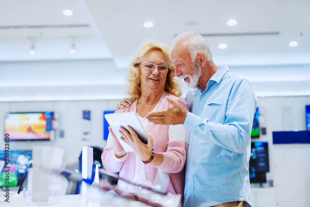 Fototapeta premium Happy smiling senior choosing new tablet while standing in tech store.