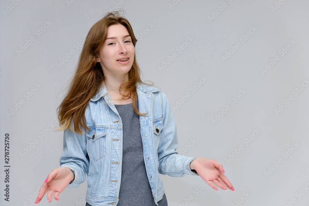 Portrait to waist of a young pretty brunette girl woman with beautiful long hair on a white background in a jacket from jeans. He talks, smiles, shows his hands with emotions in various poses. Portrait to waist of a young pretty brunette girl woman with beautiful long hair on a white background in a jacket from jeans. He talks, smiles, shows his hands with emotions in various poses.