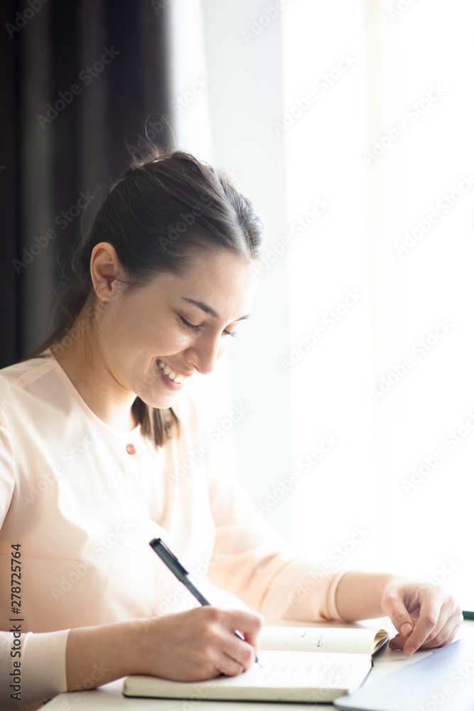 Obraz premium Smiling girl works at the table at home behind a laptop, makes notes