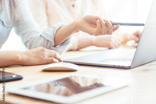 Girls dressed in casual discuss work issues, hands on a laptop