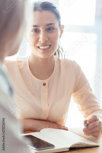 Young girl in a meeting makes notes in a notebook and smiles