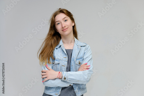 Portrait to waist of a young pretty brunette girl woman with beautiful long hair on a white background in a jacket from jeans. He talks, smiles, shows his hands with emotions in various poses.