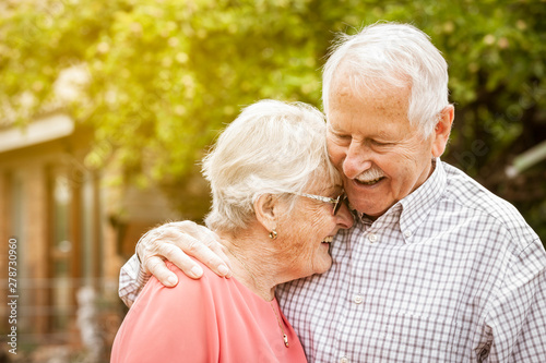 older couple are standing in the garden, hugging each other and laughing at each other photo