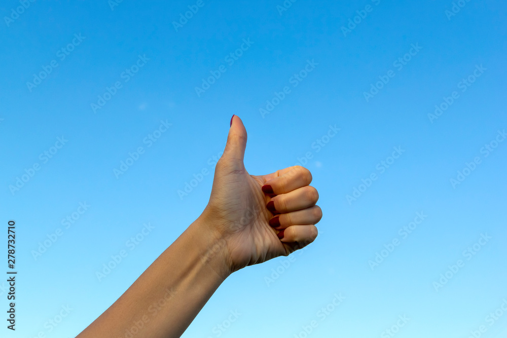 Hand gesturing thumbs up showing good or ok on blue sky background Hand gesturing thumbs up showing good or ok on blue sky background