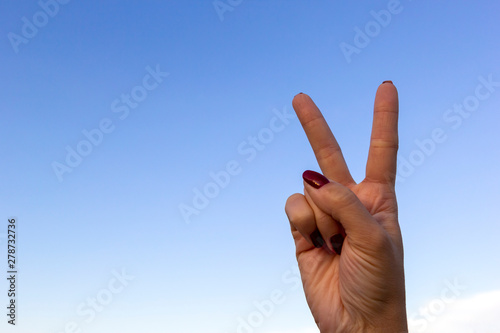 Hand gesturing peace sign or victory on blue sky background