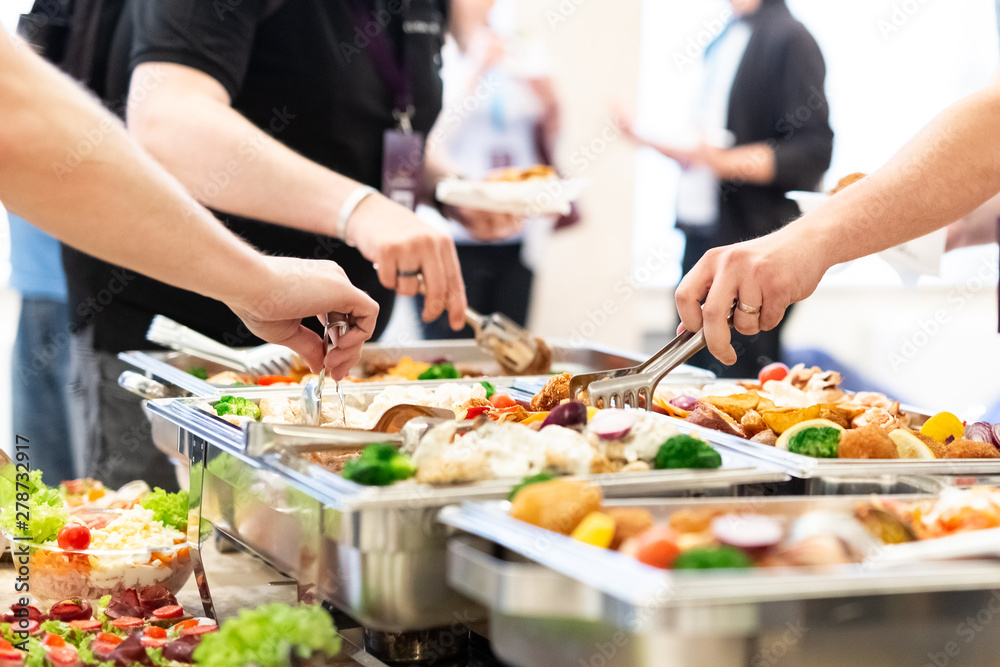 Hands picking up food from buffet catering table at the party.