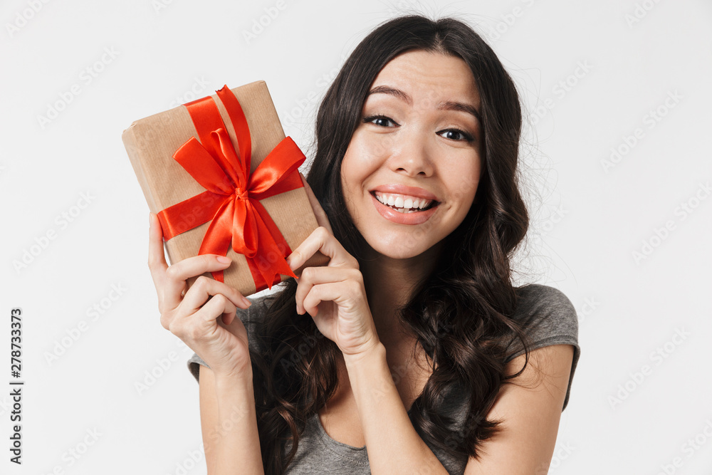Beautiful excited young woman posing isolated over white wall background holding present box. Beautiful excited young woman posing isolated over white wall background holding present box.