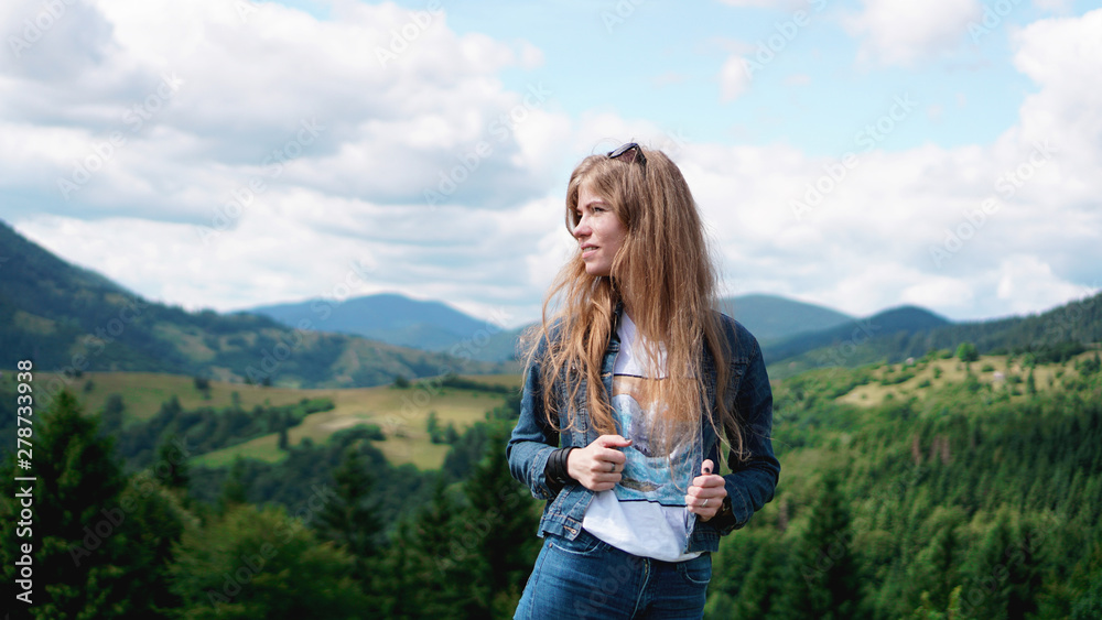Woman standing on the mountain top looking at panoramic view of mountain range under blue sky