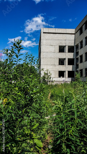 Abandoned overgrown concrete house on a sunny summer day. Building without glass windows