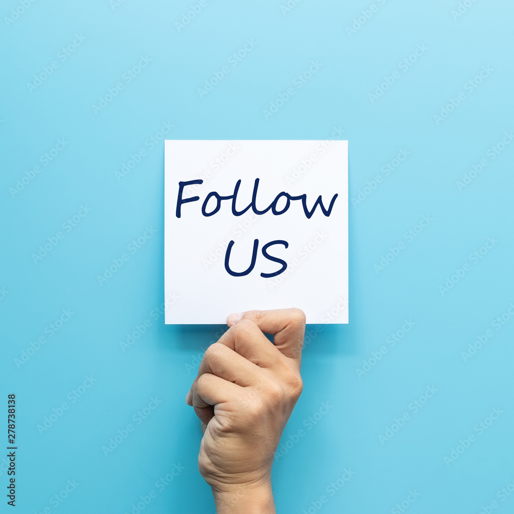 hand holding white paper with text follow us isolated on blue background. social media trend and internet marketing concept hand holding white paper with text follow us isolated on blue background. social media trend and internet marketing concept