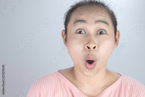 Portrait wow and surprised face of Asian young woman in pink shirt on grey background.